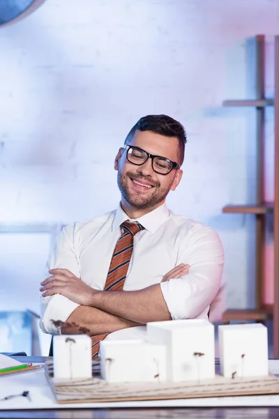 Happy architect smiling with crossed arms near architectural maquette — Stock Photo