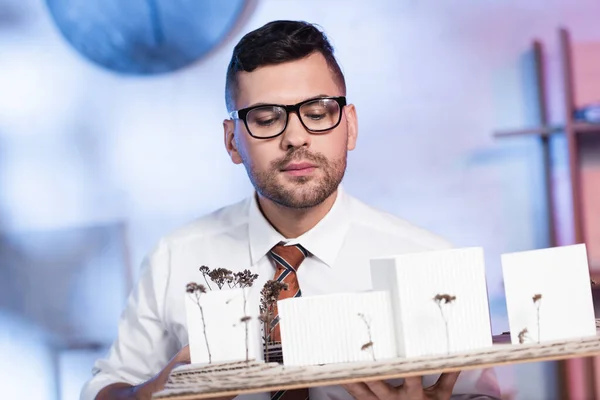 Architecte sérieux dans les lunettes regardant la maquette architecturale dans le bureau — Photo de stock