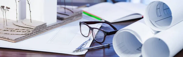 Blueprints, architectural maquette, eyeglasses and divider on desk in office, banner — Stock Photo