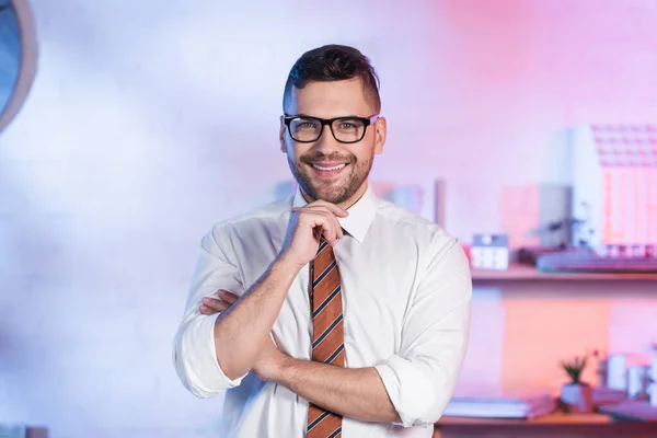 Happy architect in eyeglasses looking at camera while standing in office — Stock Photo