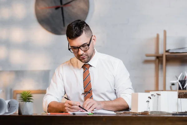 Focused architect working near houses models in architectural agency — Stock Photo