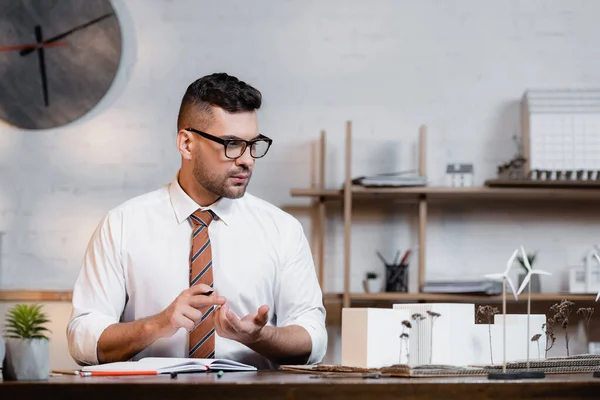 Arquitecto contando con dedos cerca de casas modelos en el lugar de trabajo - foto de stock