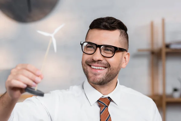 Arquitecto alegre en gafas sonriendo mientras sostiene el modelo de turbina eólica - foto de stock