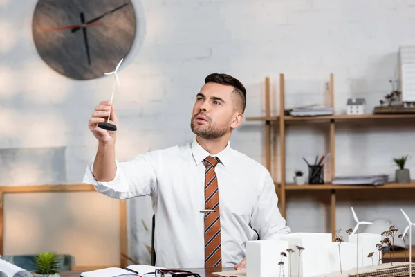 Architect holding model of wind generator near architectural project at workplace — Stock Photo