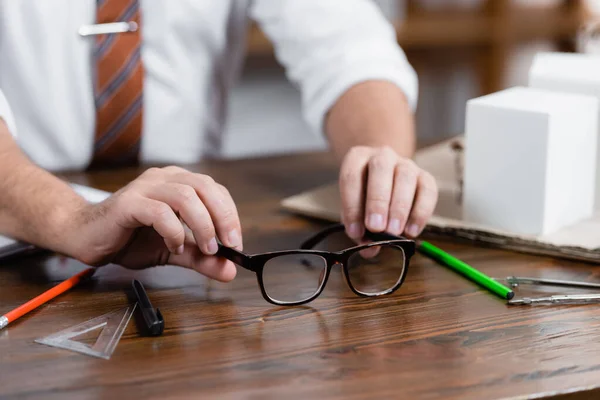 Vue recadrée de l'architecte près des lunettes sur un bureau en bois, fond flou — Photo de stock