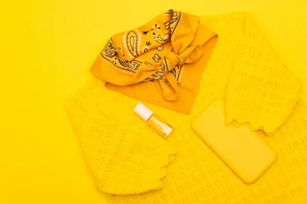 Верхний вид шарфа с орнаментом на одежде со смартфоном в случае и лак для ногтей изолирован на желтый — стоковое фото