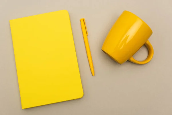 Vista dall'alto del quaderno giallo vicino alla penna e tazza vuota isolata su grigio — Foto stock