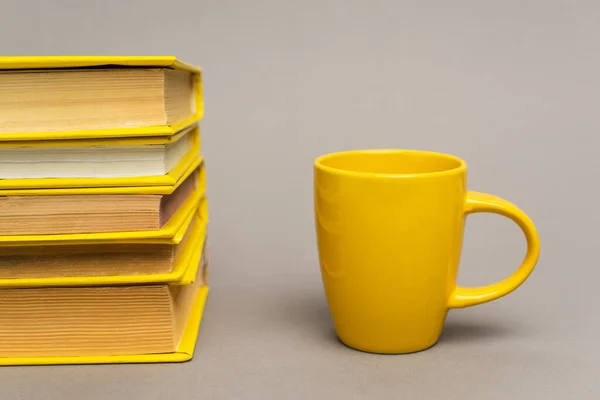 Pila de cuadernos amarillos cerca de taza en gris - foto de stock