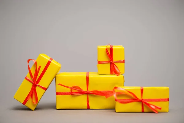 Загорнуті жовті подарунки з червоними стрічками на сірому — стокове фото