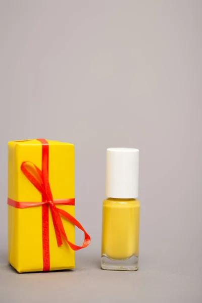 Caixa de presente amarelo envolto perto de garrafa com esmalte isolado em cinza — Fotografia de Stock