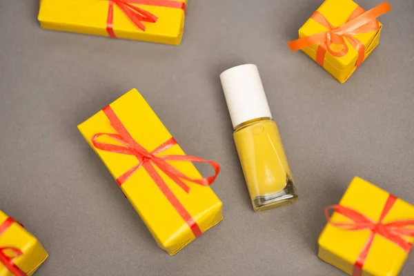 Vue grand angle des boîtes-cadeaux jaunes enveloppées près de la bouteille avec vernis à ongles sur gris — Photo de stock