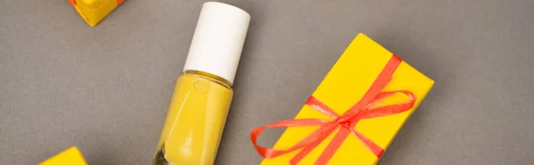 Vista de ángulo alto de la caja de regalo amarilla envuelta cerca de la botella con esmalte de uñas en gris, bandera - foto de stock