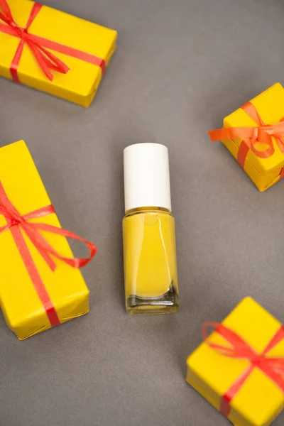 Ansicht von verpackten Geschenkboxen in Flaschennähe mit gelbem Nagellack auf grau — Stockfoto