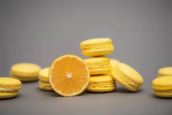 Deliciosos macarons amarelos perto da metade do limão suculento no fundo cinza — Fotografia de Stock