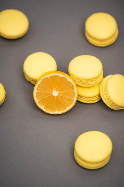 Vista de alto ângulo de deliciosos macarons amarelos perto da metade do limão suculento no fundo cinza — Fotografia de Stock