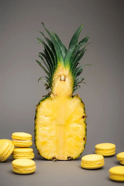 Moitié d'ananas mûrs et frais près de macarons jaunes sur fond gris — Photo de stock