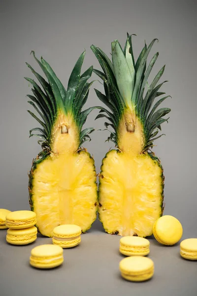 Halves of juicy pineapples and yellow macarons on grey — Stock Photo