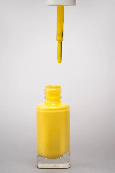 Bouteille avec vernis à ongles jaune et pinceau sur fond gris — Photo de stock