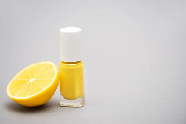 Bottle with yellow nail polish and half of lemon on grey background — Stock Photo