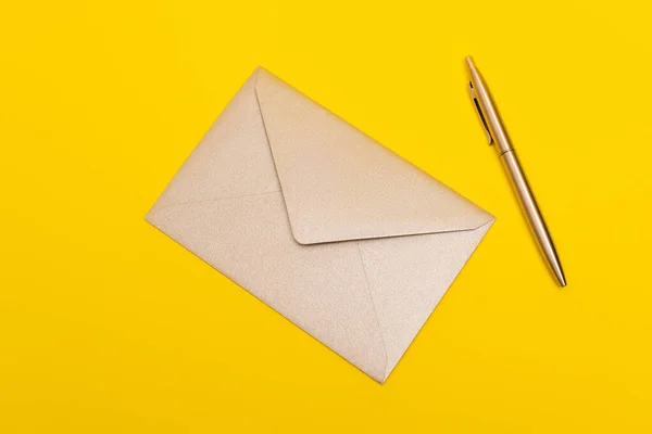 Ansicht des Umschlags in der Nähe von goldenem Stift isoliert auf gelb — Stockfoto