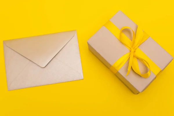 Top view of envelope near wrapped present isolated on yellow — Stock Photo