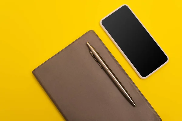 Vista dall'alto dello smartphone con schermo bianco vicino al libro delle copie e penna dorata isolata sul giallo — Foto stock
