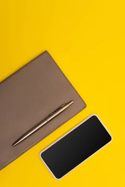 Top view of mobile phone with blank screen near copy book and golden pen isolated on yellow — Stock Photo