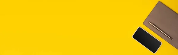 Top view of mobile phone with blank screen near copy book and golden pen isolated on yellow, banner — Stock Photo