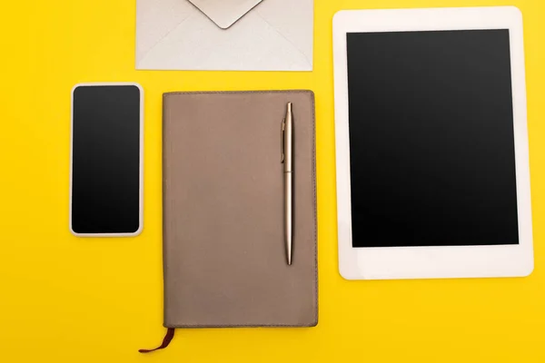 Vista superior de gadgets con pantalla en blanco cerca del libro de copias con pluma de oro cerca de sobre aislado en amarillo - foto de stock