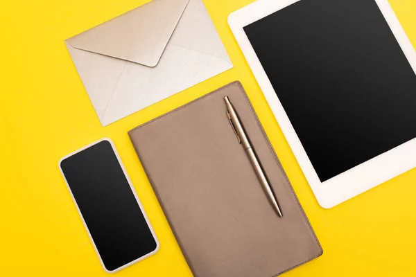 Top view of devices with blank screen near copy book with golden pen near envelope  isolated on yellow — Stock Photo