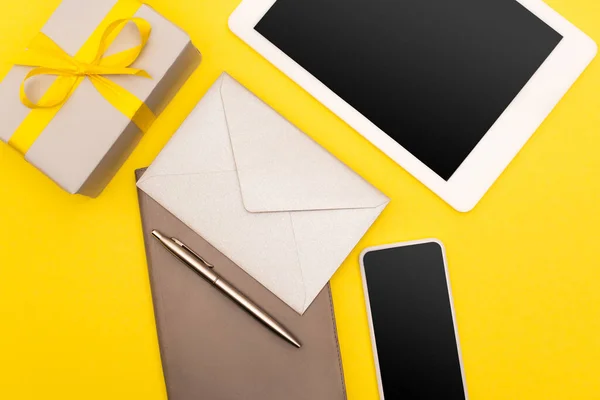 Top view of gadgets with blank screen, copy book with golden pen and envelope near present isolated on yellow — Stock Photo