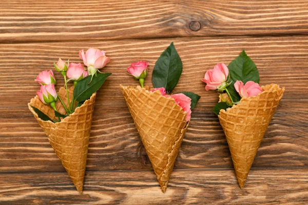 Vue de dessus des roses de thé rose avec des feuilles dans des cônes de gaufre sur la surface en bois — Photo de stock