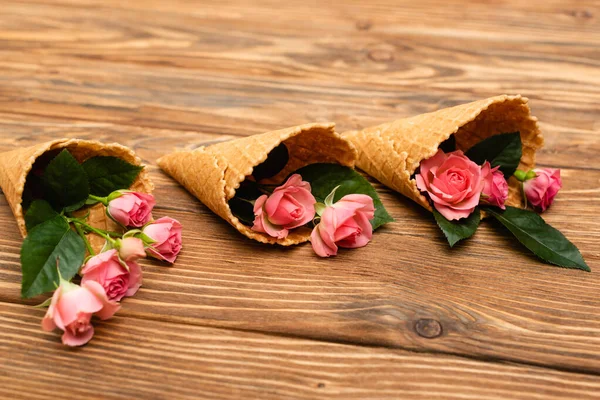 Rosas de chá rosa em cones de waffle na superfície de madeira — Fotografia de Stock