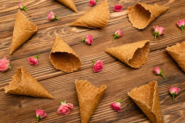 Vista de ángulo alto de rosas rosadas de té cerca de conos de waffle en la superficie de madera - foto de stock