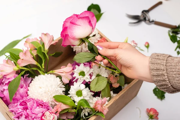 Vista recortada de la mujer sosteniendo flores rosadas cerca de la caja de madera en blanco - foto de stock