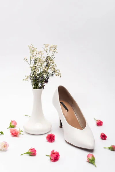 Female shoe near tea roses and vase with flowers on white — Stock Photo