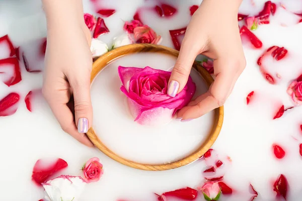 Abgeschnittene Ansicht einer Frau mit einer hölzernen Schale mit rosa Pfingstrose in der Nähe von Blumen im milchigen Wasser — Stockfoto