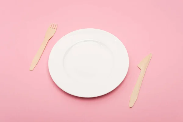 Disposable wooden cutlery near white plate isolated on pink — Stock Photo