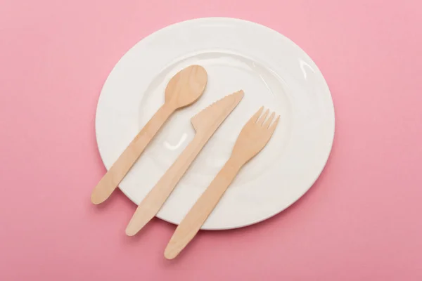 Top view of disposable wooden cutlery on white plate isolated on pink — Stock Photo