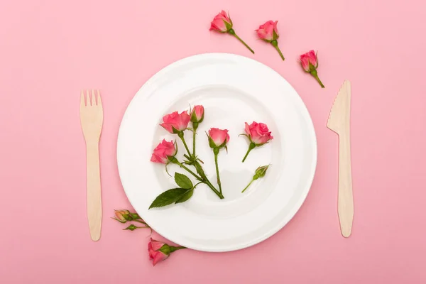 Top view of disposable wooden cutlery near white plate with flowers isolated on pink — Stock Photo