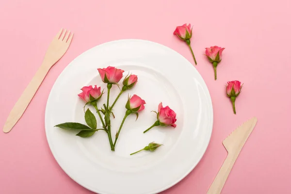 Top view of wooden cutlery near white plate with flowers isolated on pink — Stock Photo