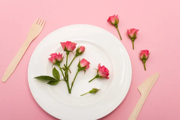 Vue de dessus des couverts en bois près de la plaque blanche avec des fleurs isolées sur rose — Photo de stock