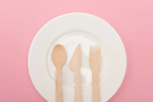 Top view of disposable wooden cutlery on plate isolated on pink — Stock Photo