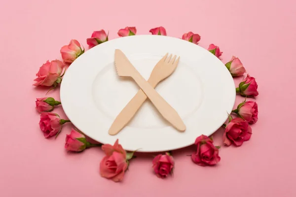 Couché plat avec des couverts en bois jetables près de la plaque blanche et des roses de thé isolés sur rose — Photo de stock