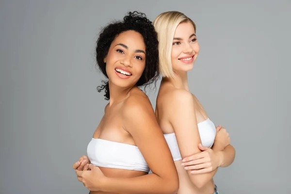 Multicultural women in white tops smiling isolated on grey — Stock Photo