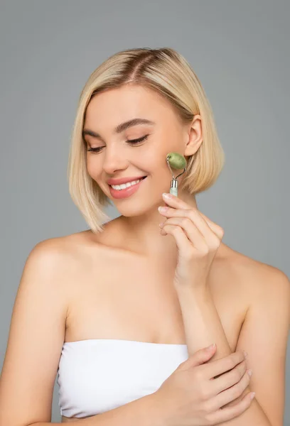 Smiling woman in white top using jade roller isolated on grey — Stock Photo
