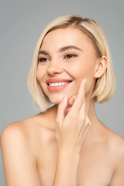 Jeune femme aux épaules nues appliquant de la crème sur le visage isolé sur gris — Photo de stock