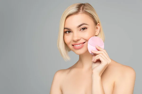 Blonde woman with naked shoulders holding silicone cleanser isolated on grey — Stock Photo