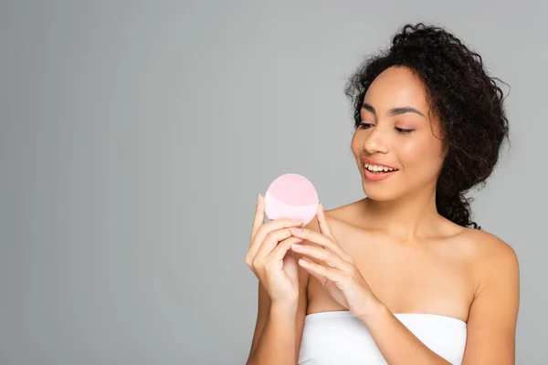Smiling african american woman holding silicone cleanser isolated on grey — Stock Photo