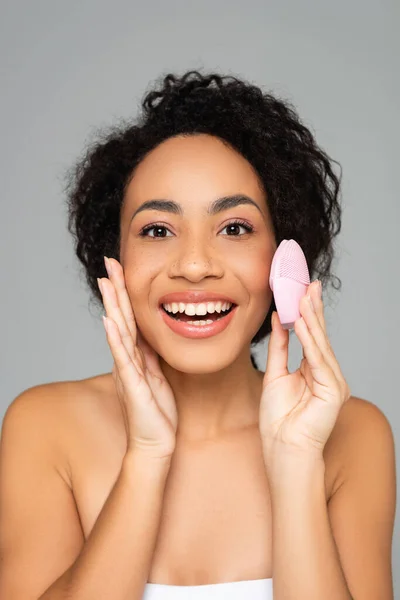 Mujer americana africana alegre con piel perfecta sosteniendo cepillo de silicona aislado en gris — Stock Photo